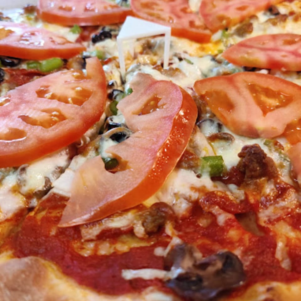 Close-up of a Pioneer Pizza with sliced tomatoes, green peppers, and sausage.