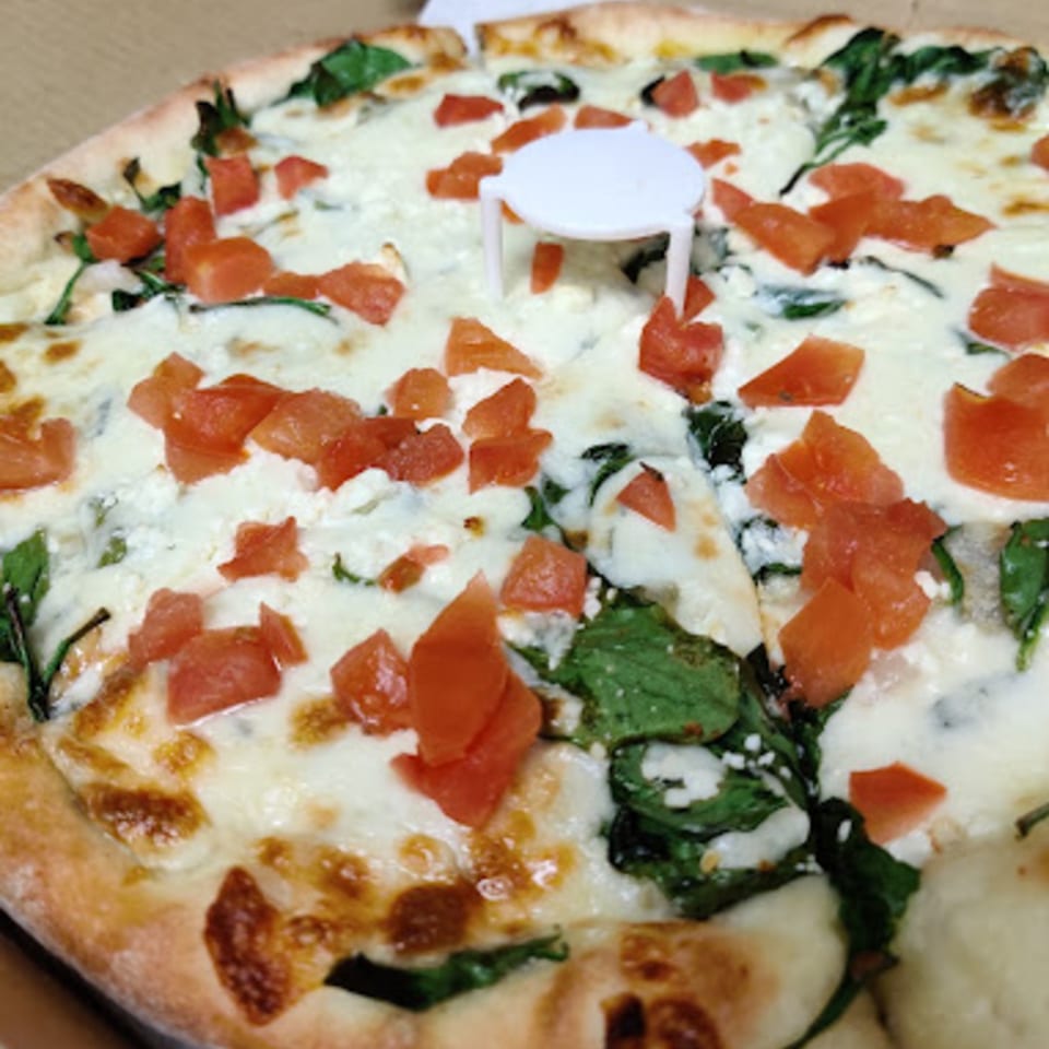 Pioneer Pizza's white pizza with spinach and diced tomatoes, featuring a pizza saver in the center.
