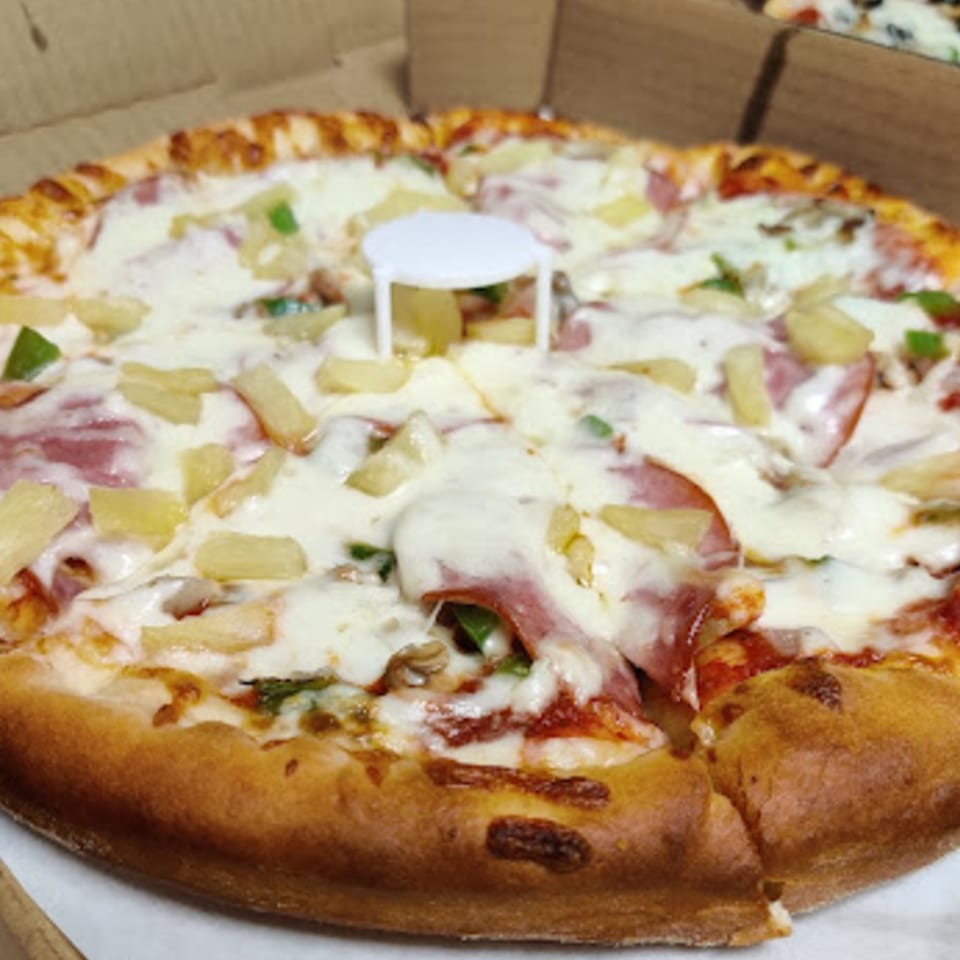 A Pioneer Pizza Hawaiian pizza with ham, pineapple, and green peppers in a cardboard box.