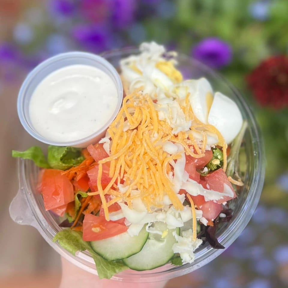 A fresh garden salad with tomatoes, cucumbers, shredded cheese, and hard-boiled eggs, with ranch dressing.
